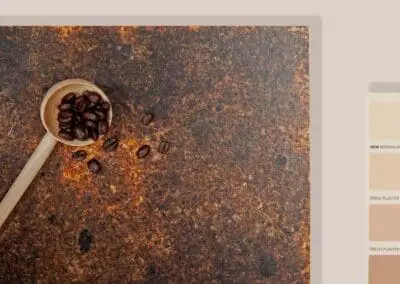 A mood board of a Kava husk sample. Next to it shows part of a colour chart with soft warm red toned whites to brown to red. On top of the sample sits a wooden spoon with coffee beans in and slightly spilled over. A copper door handle also sits on the sample. Above the husk kava sample is a hemp material sample. The background is a soft warm red-white.